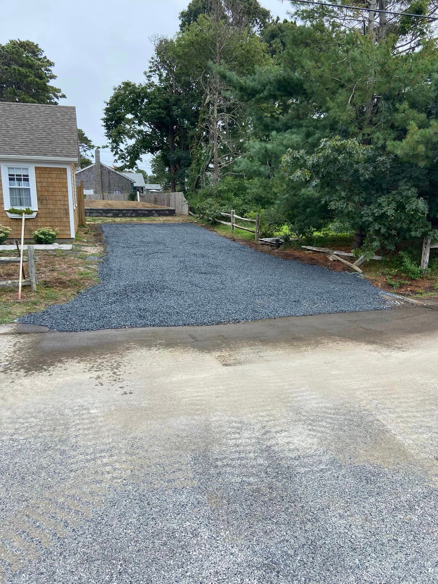 Gravel driveway leading to a building with a blue gravel extension and a tree on the right.