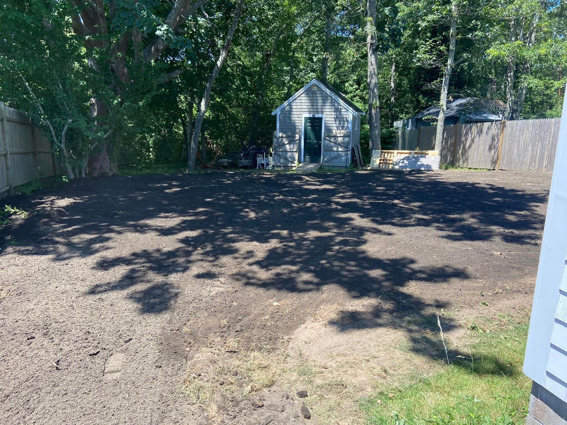 A backyard with freshly turned dark soil, small shed, and trees. Shadows cast across the ground.