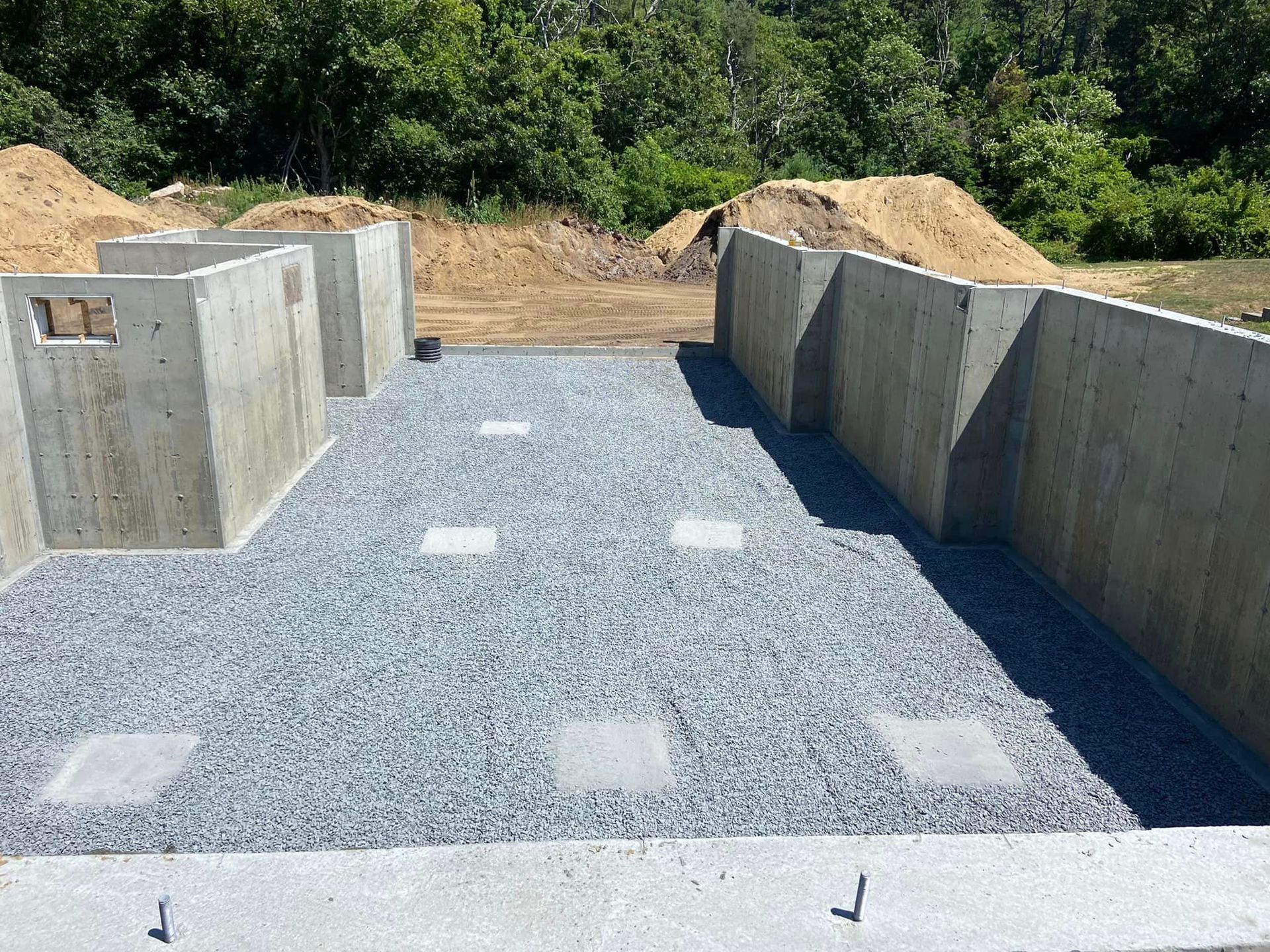 Concrete foundation walls and gravel-filled base for a building, with a dirt pile in the background.