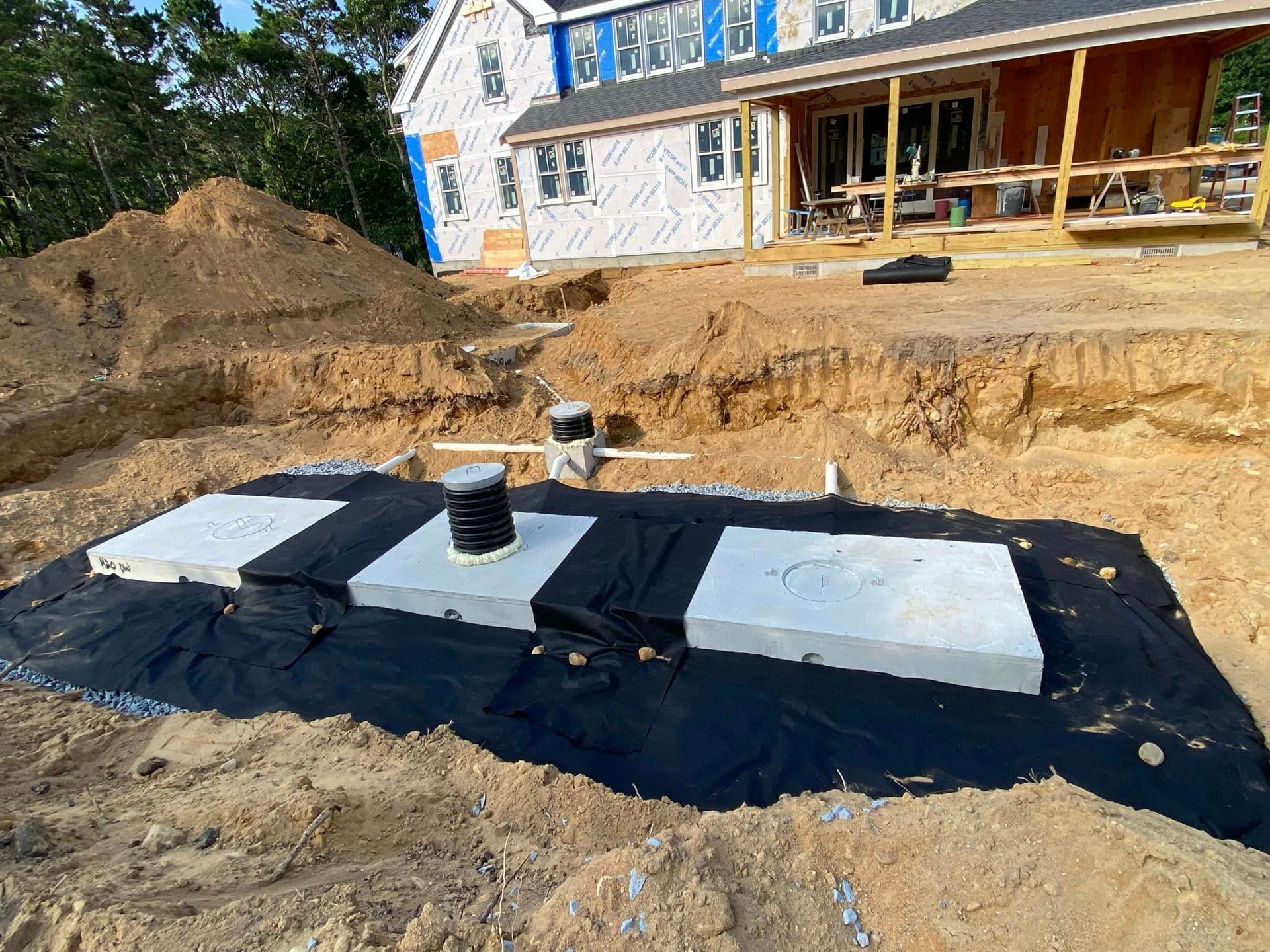 Construction site with concrete septic tank components laid out; dirt mound, house in background.