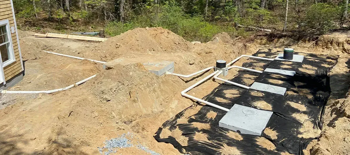 A septic system under construction in a sandy area. White pipes connect several concrete boxes.