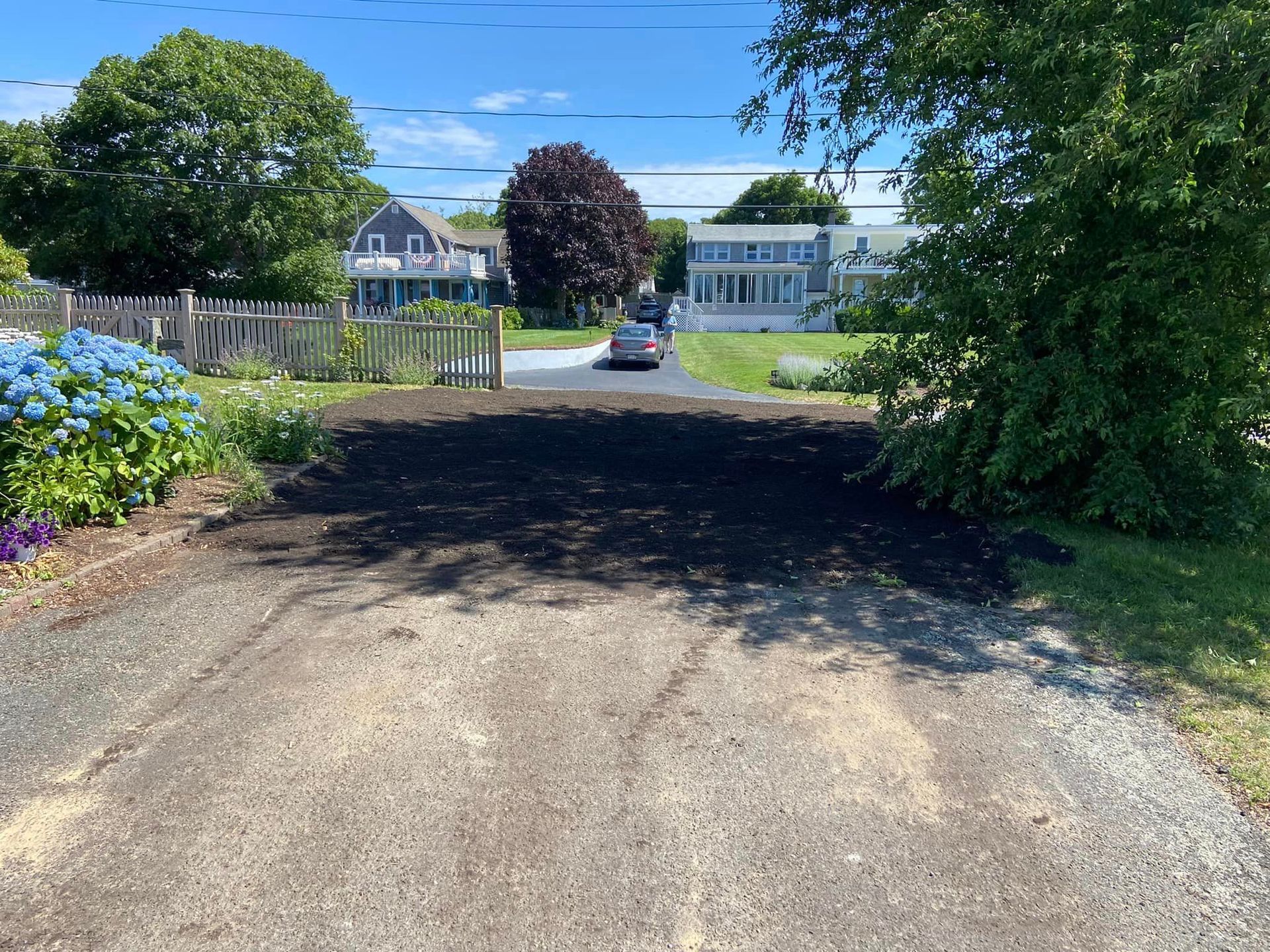 Driveway with fresh dark mulch leading toward houses on a sunny day.