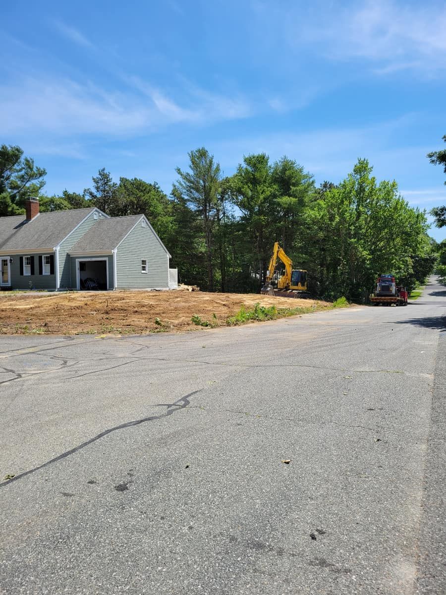 A house with an unfinished driveway, construction equipment, and trees on a sunny day.