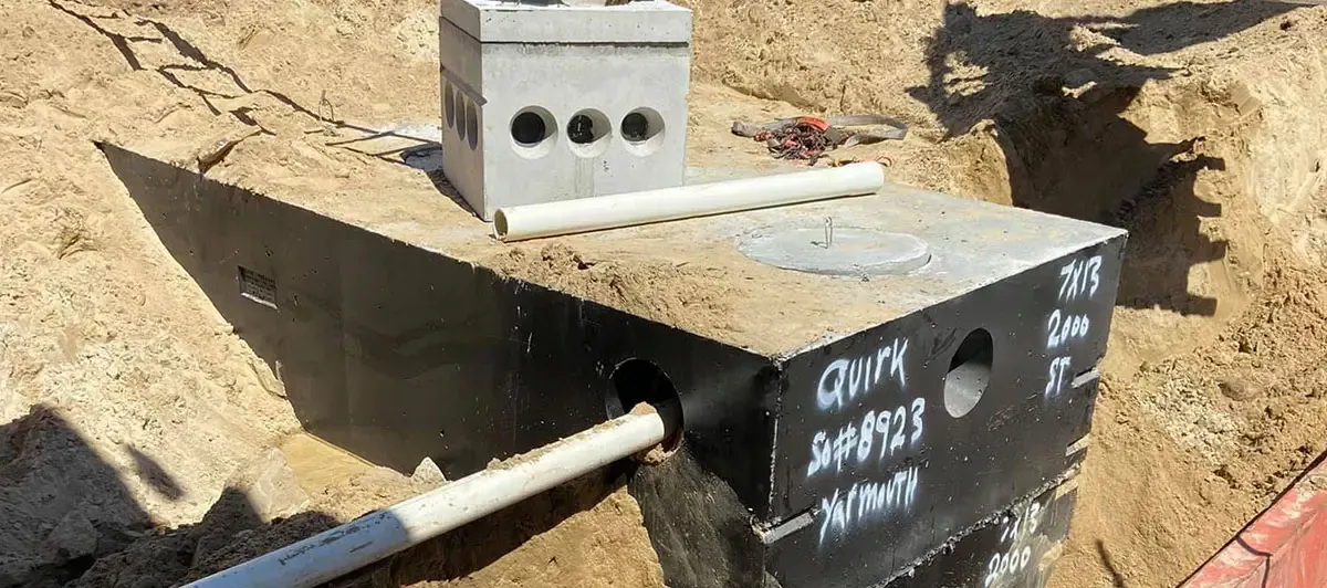 A septic tank installation, with pipes and a concrete block structure in a sandy trench.
