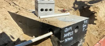 A septic system is partially buried. A black rectangular tank and a concrete block are visible with connecting pipes.