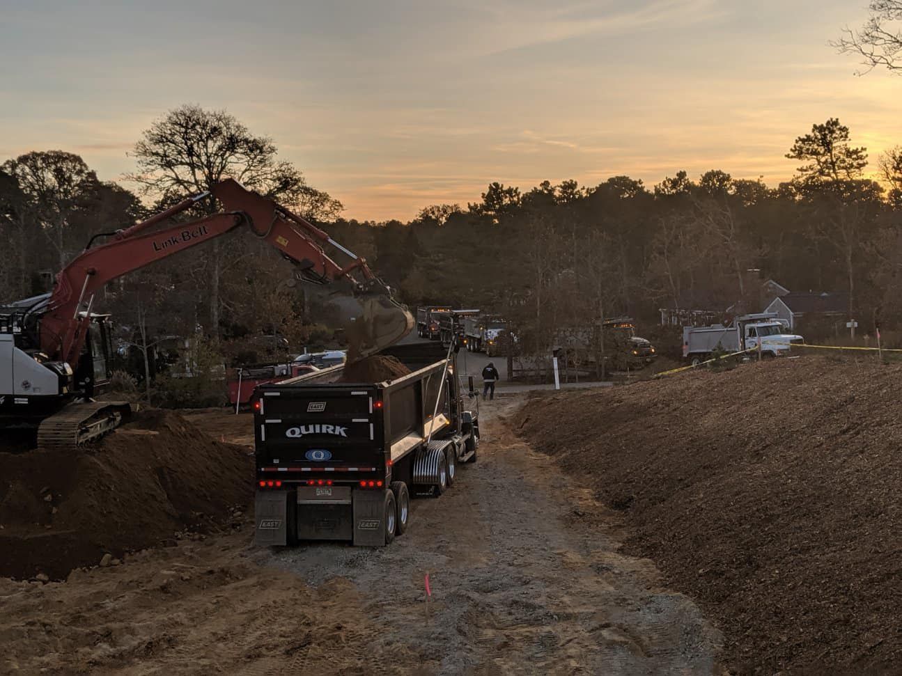 Dump truck on a dirt road, excavator in the background, construction site at sunset.