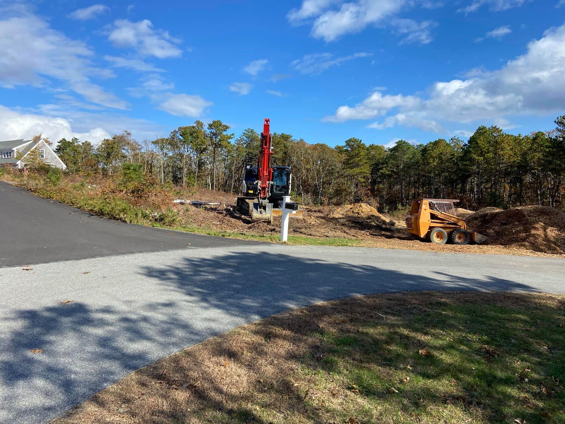 Construction site with excavator and skid steer clearing brush, blue sky.