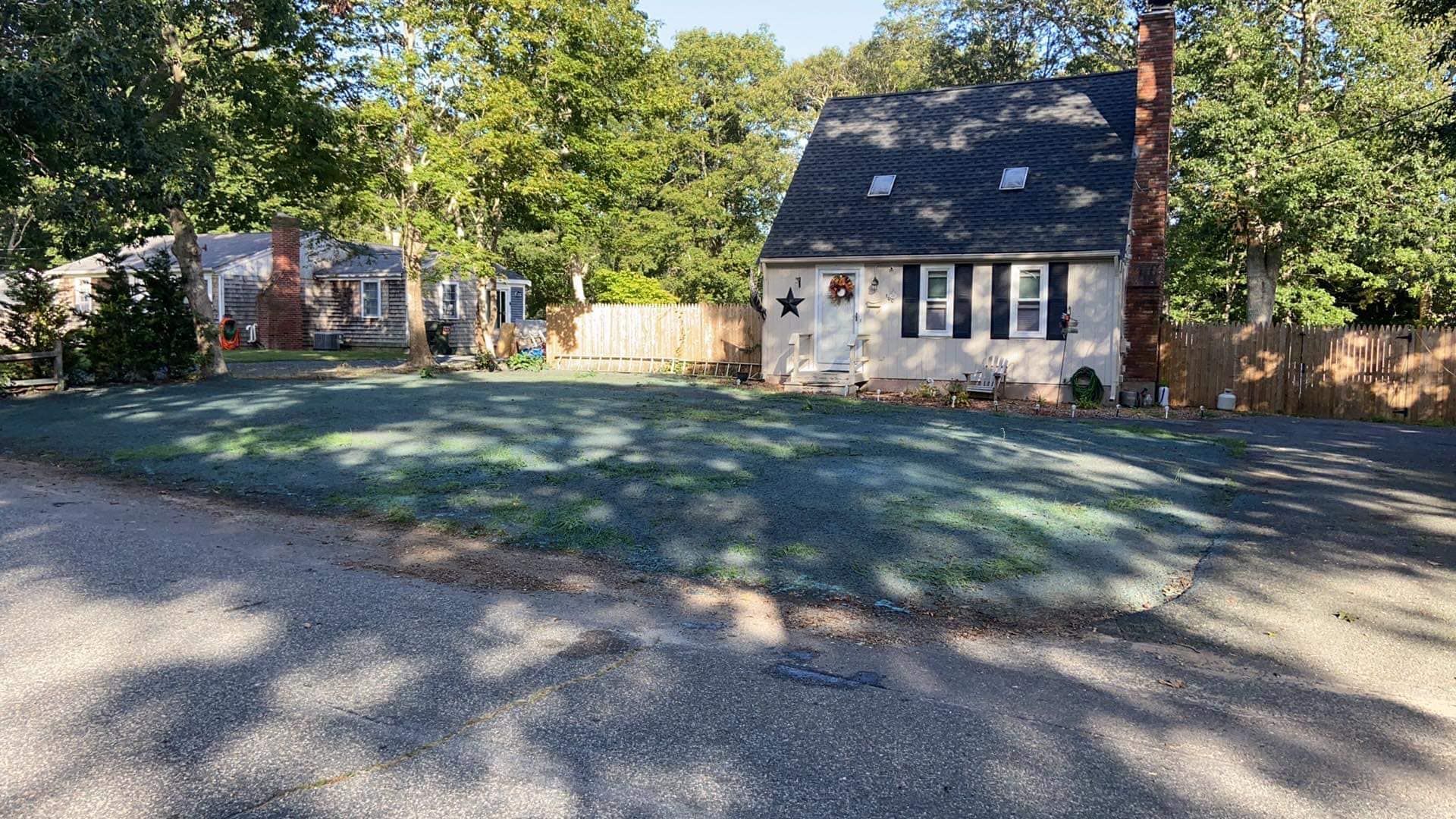 A house with black shutters, a lawn, and a road on a sunny day.