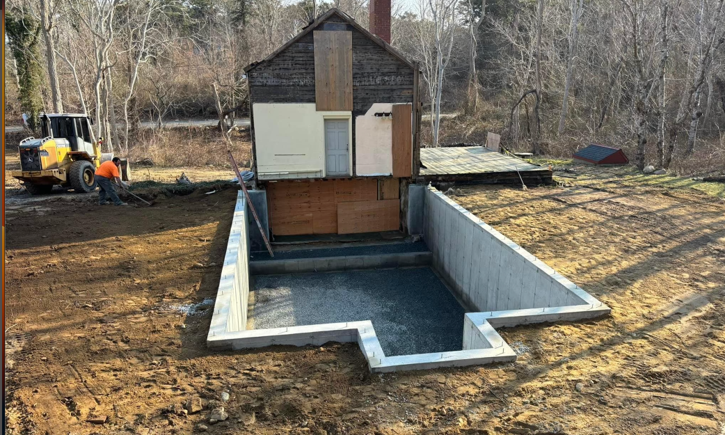 Construction site with a concrete foundation, unfinished building, and excavator.
