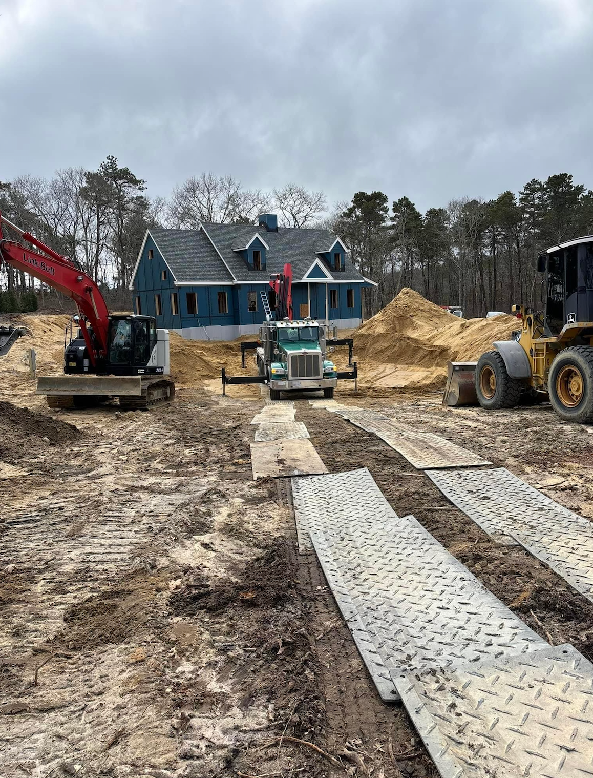 Construction site with machinery, a blue house under construction, and dirt.