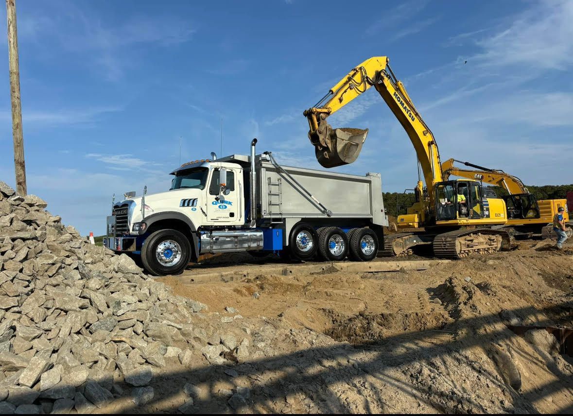 A yellow excavator loading a white dump truck with gravel on a construction site under a blue sky.