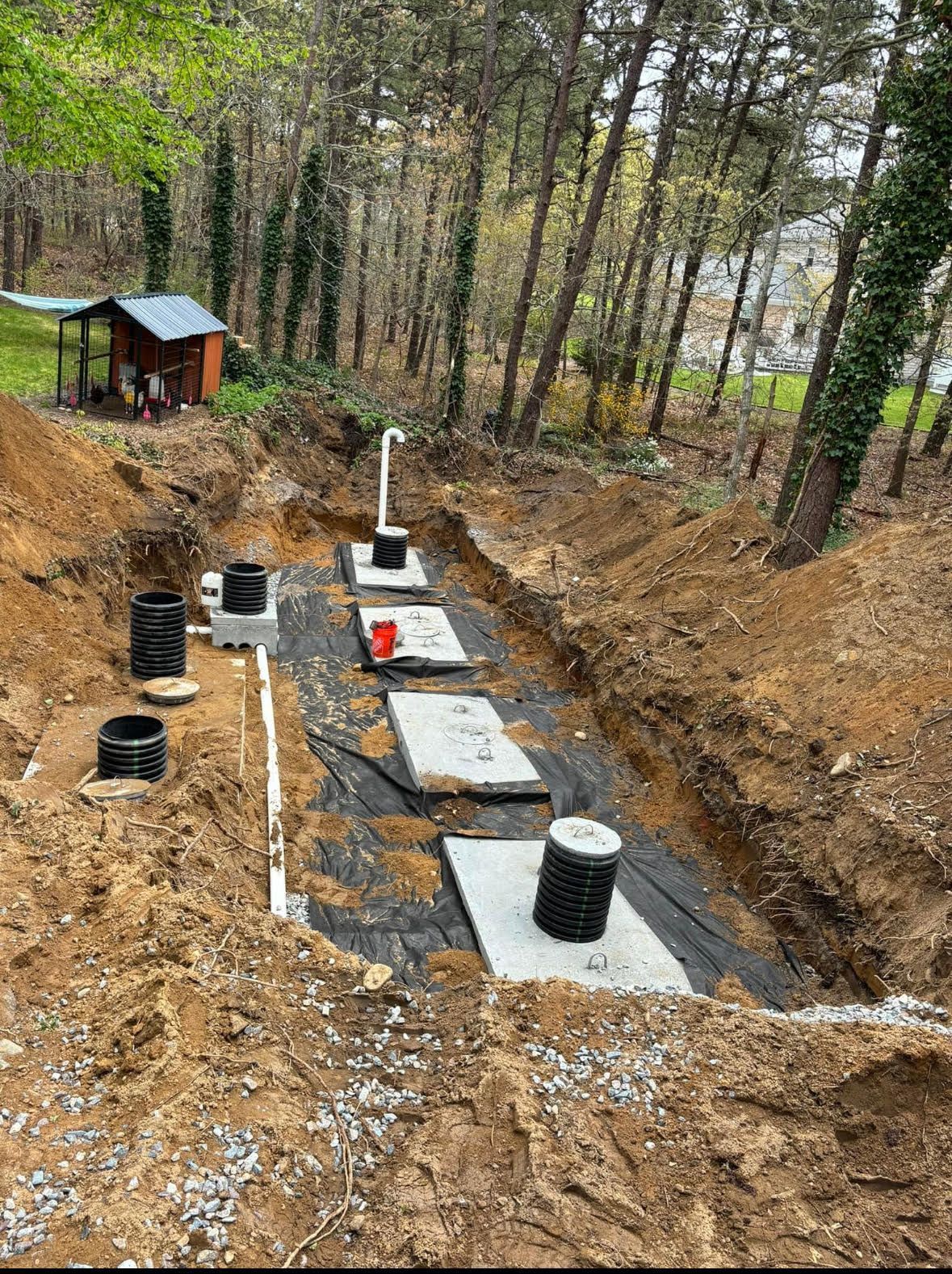 Excavated area for a septic system installation. Gray tanks and white pipes are in a trench of dirt.