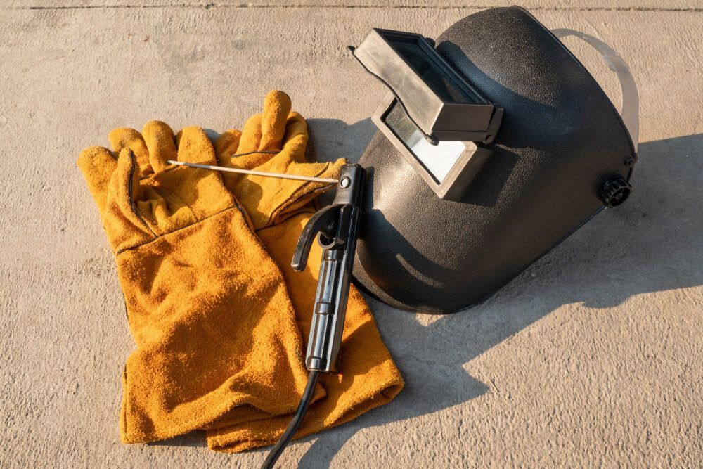 A Welding Helmet , Gloves , And An Electrode Are On The Ground — Summerland Tool Supplies In Casino, NSW