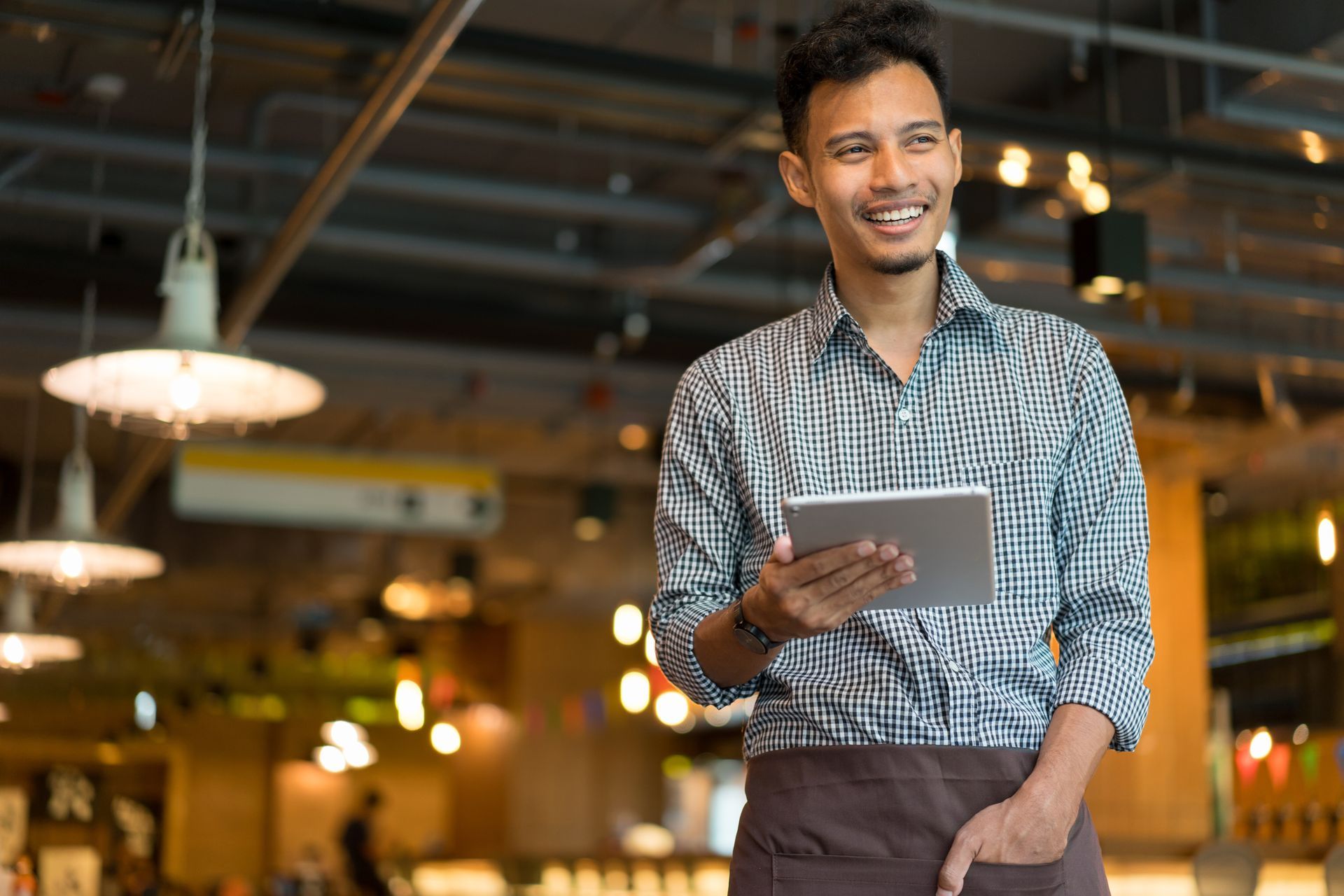 A man holding a tablet on a blurred, lighted shop background.