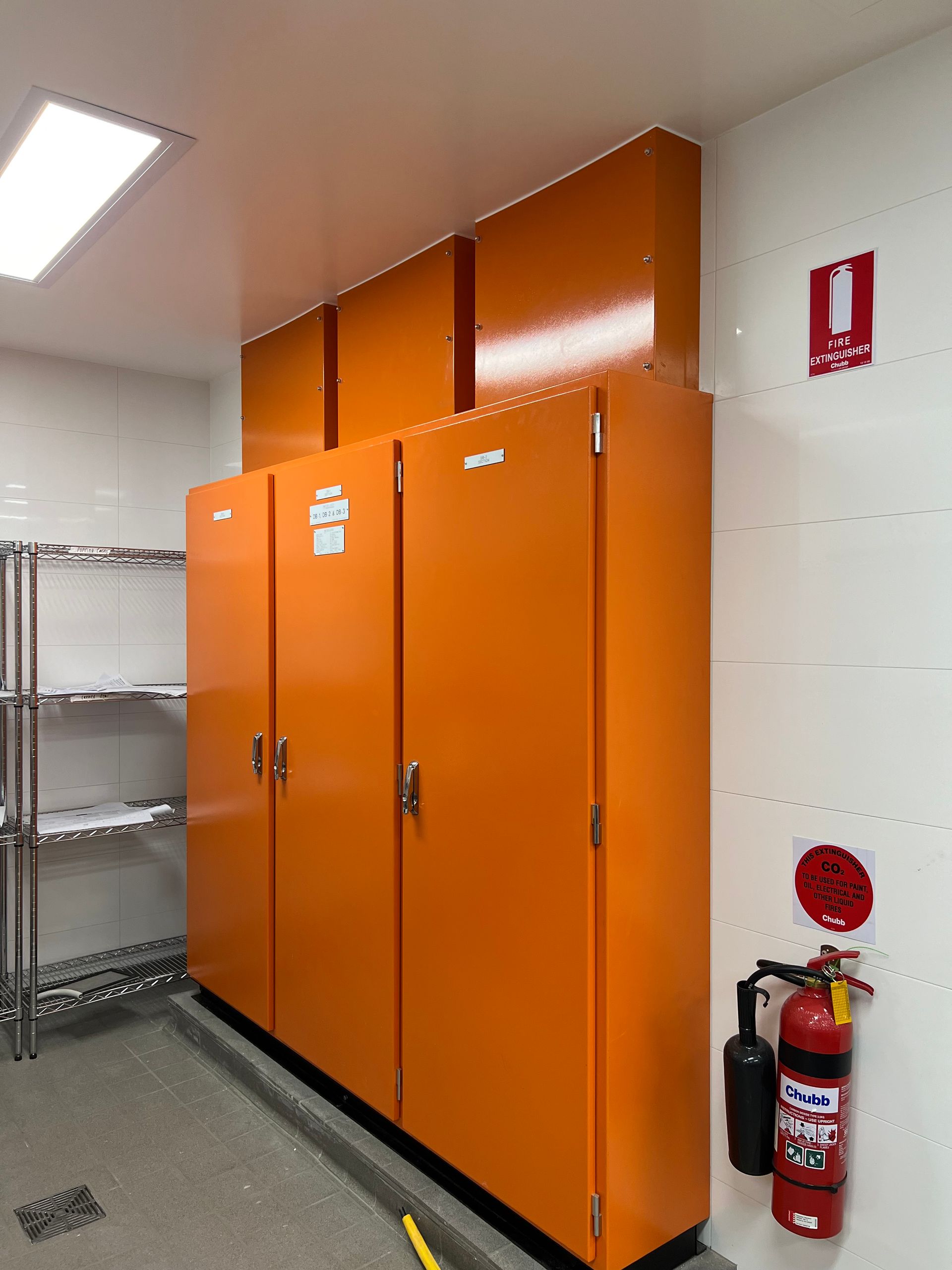 Orange electrical cabinets against a white wall in a room, with a fire extinguisher.