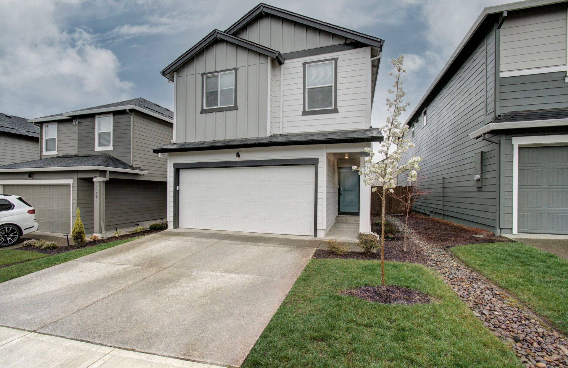Suburban two-story house with white garage, concrete driveway, and small front yard with a young tree