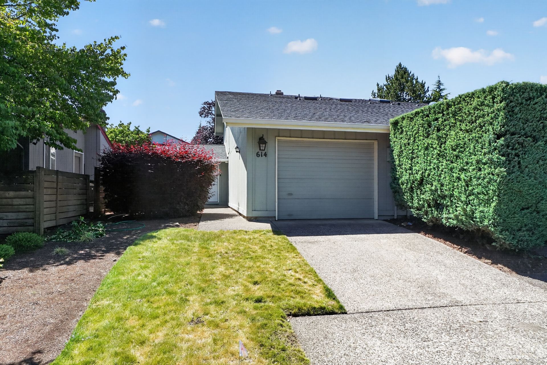 Single-car garage with a white door, driveway, and green hedges beside a narrow lawn.