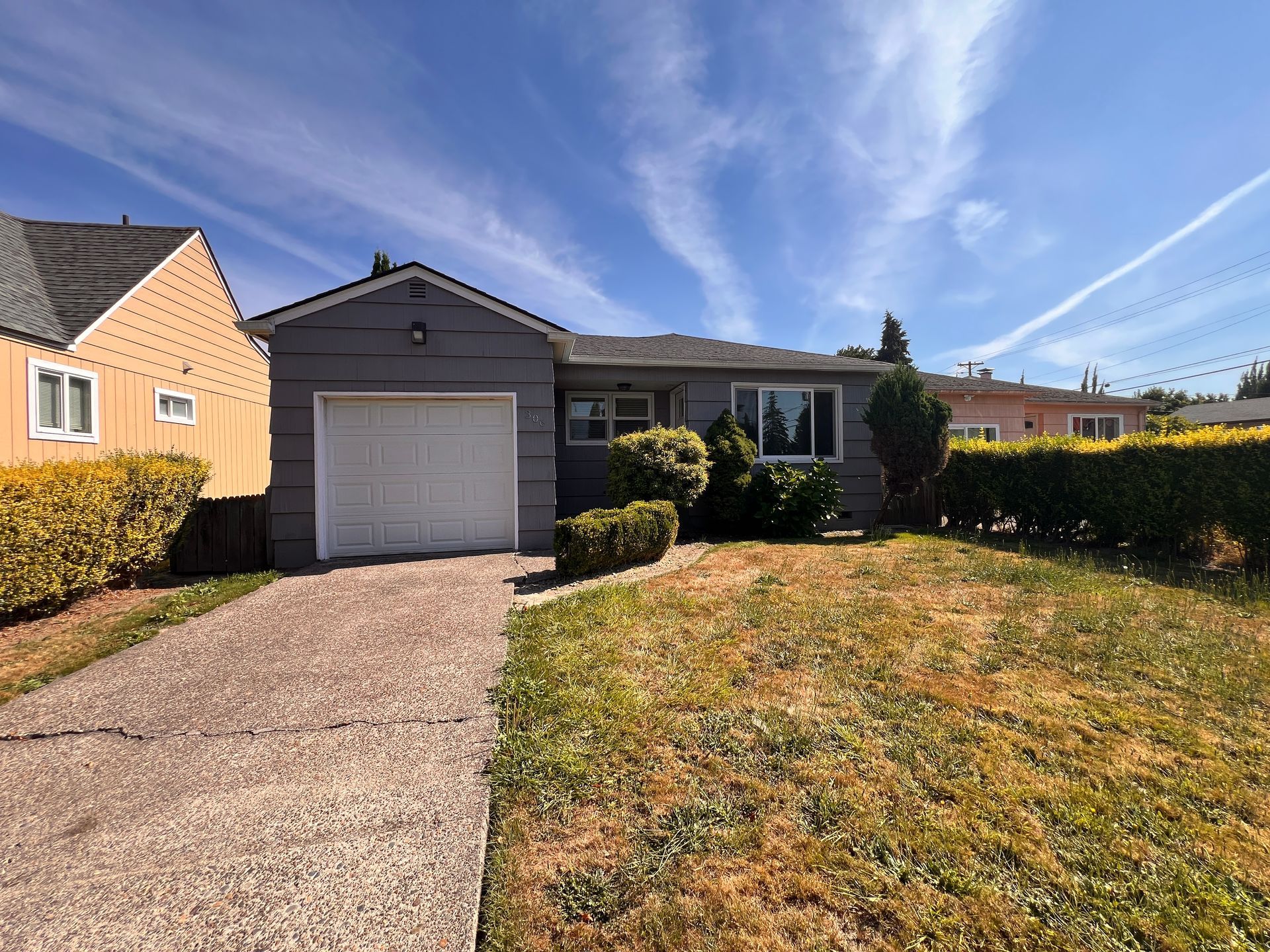 Single-story house with a garage, driveway, and front lawn under a blue sky