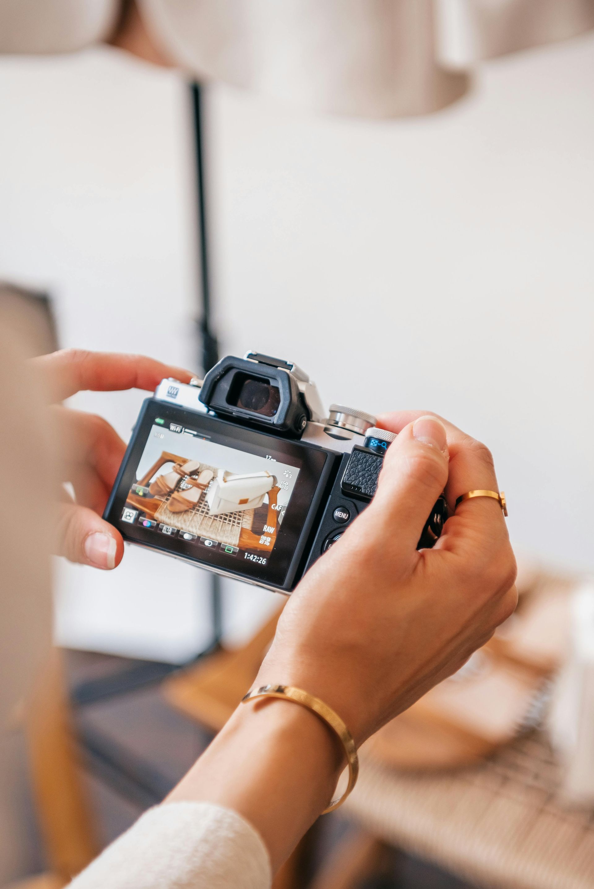 Person holding a digital camera, taking a photo of a still life setting with items on a table.