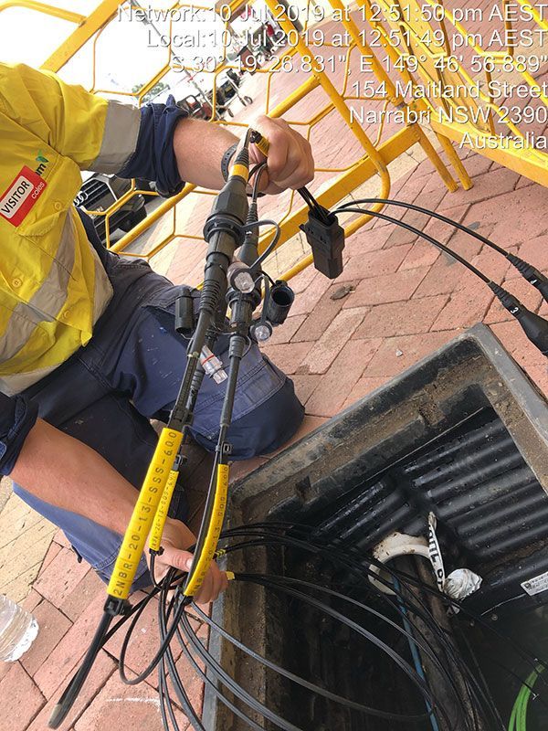 A man is kneeling down in a manhole cover holding a pair of pliers.