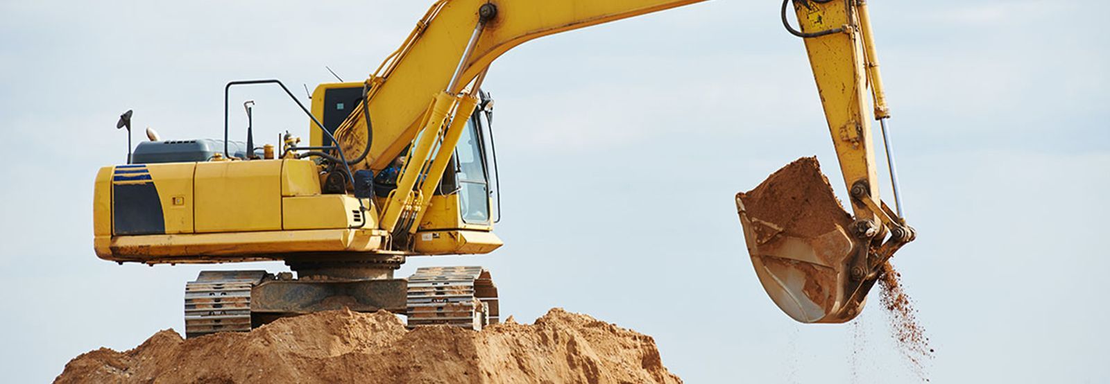 A yellow excavator is digging a pile of dirt.