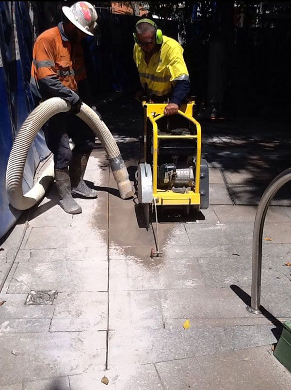 Two men are using a yellow machine to cut concrete