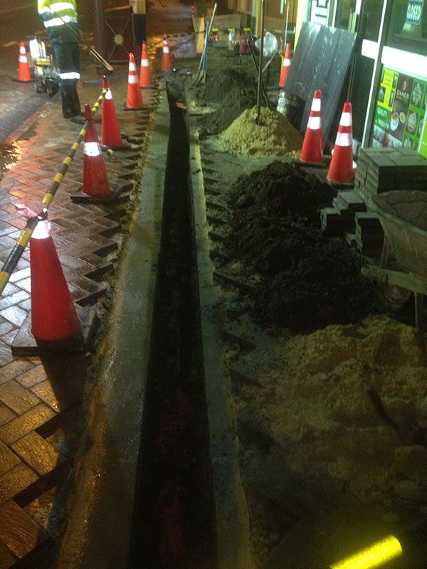 A man is digging a trench on the side of the road.