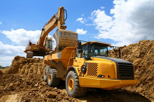A yellow dump truck is being loaded with dirt by an excavator.