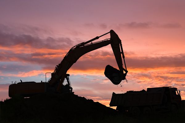 An excavator is loading dirt into a dump truck at sunset