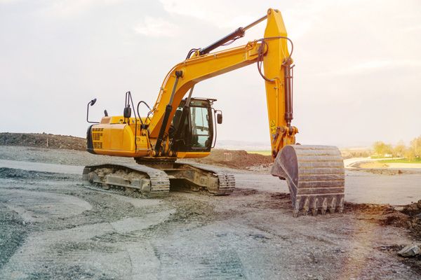 A yellow excavator is sitting on top of a dirt field.