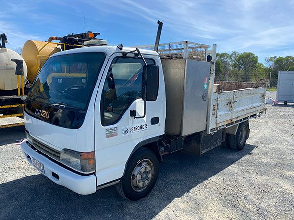 A white truck with a stainless steel box on the back is parked in a gravel lot.