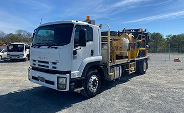 A white and yellow truck is parked in a gravel lot.