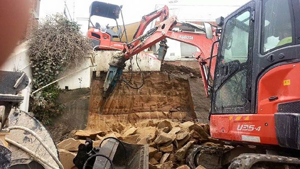 A red and black excavator is digging a hole in a pile of rocks.