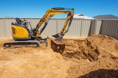 A yellow excavator is digging a hole in the ground.