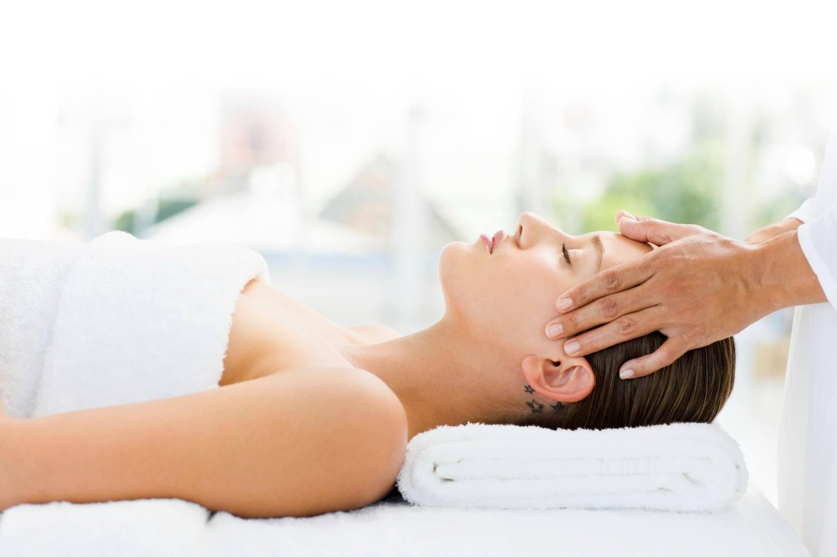 Hands gently pressing a person's forehead during a spa massage, eyes closed.