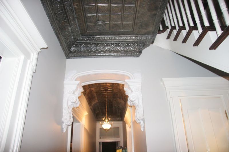 Ornate hallway with carved ceiling, white walls, and a staircase railing overhead
