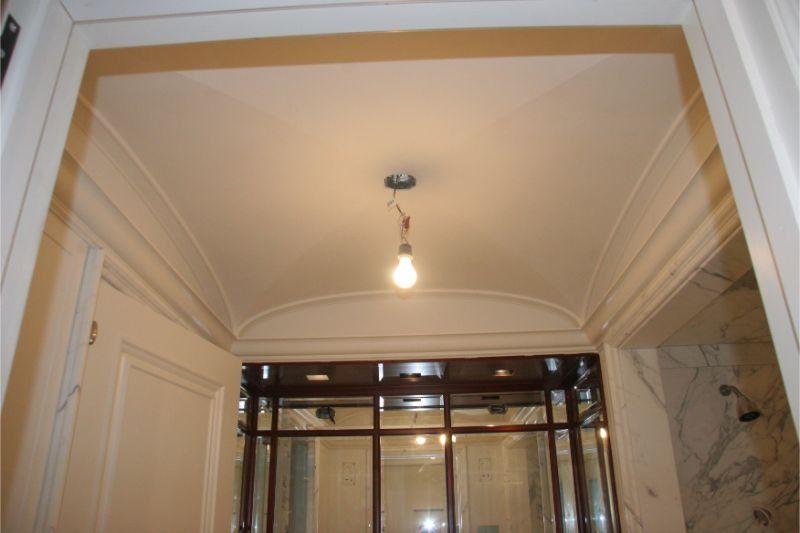 White hallway ceiling with decorative molding, a hanging light bulb, and a glass doorway below