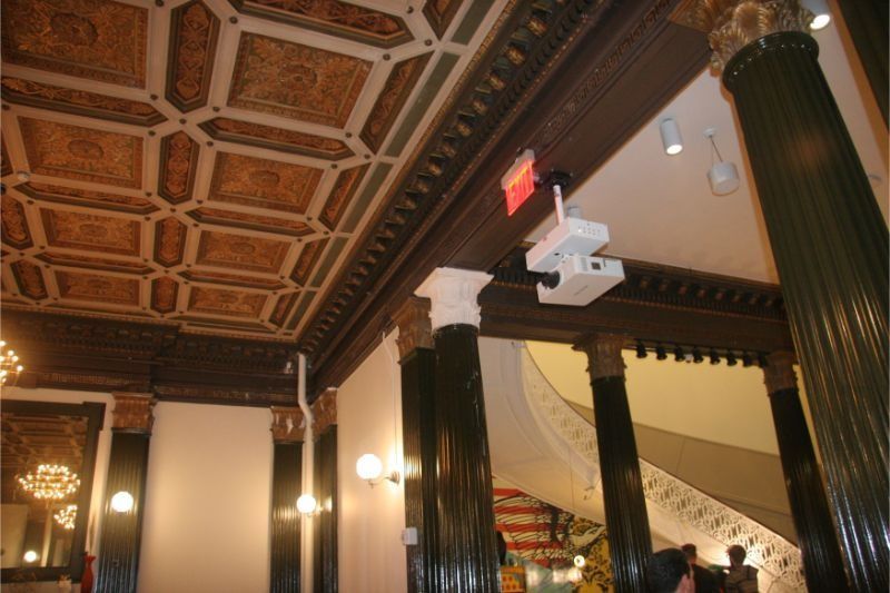 Interior with ornate coffered ceiling, dark columns, and warm wall lights in a historic-style room