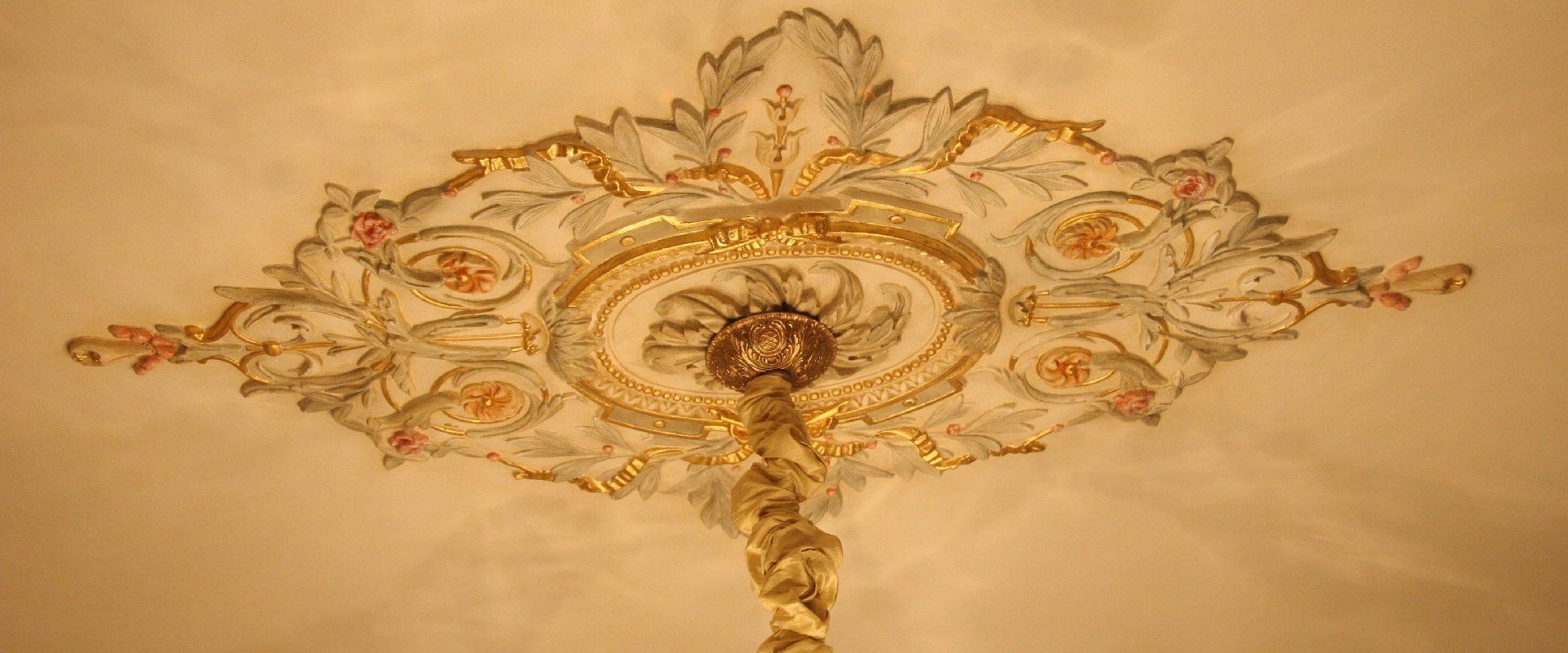 Ornate gold and cream ceiling medallion with a central chandelier mount and decorative floral patterns