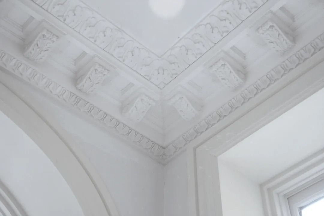 White ornate ceiling corner with decorative plaster molding and a window