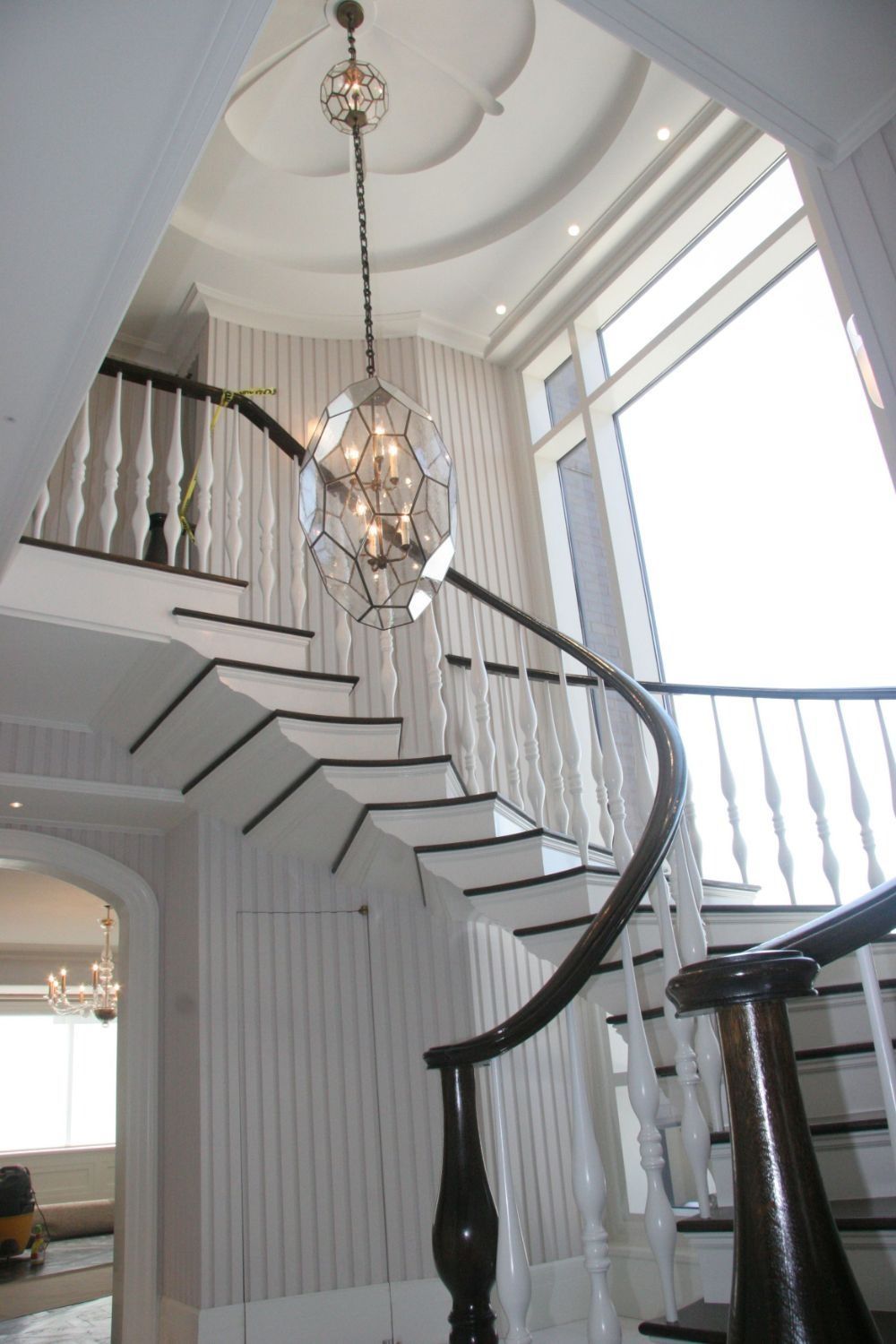 Elegant curved staircase in a bright foyer with white walls and a hanging chandelier