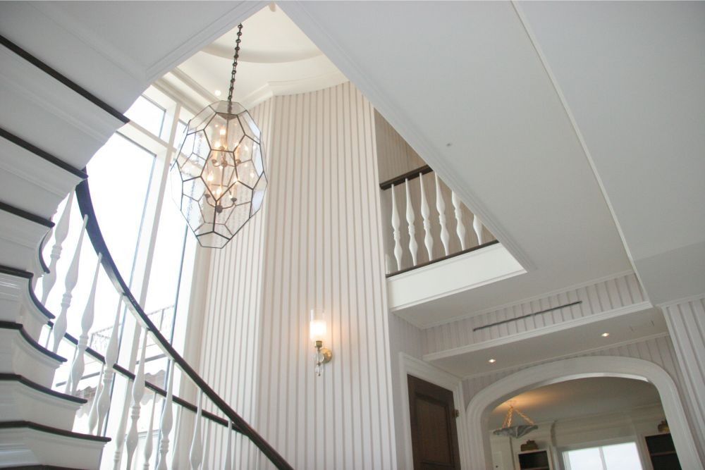 Elegant white staircase with curved railing, chandelier, and striped wall in a bright foyer