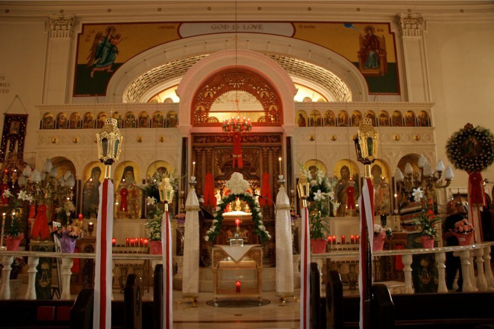 Ornate church altar with statues, candles, and gold decorations beneath a red arched canopy