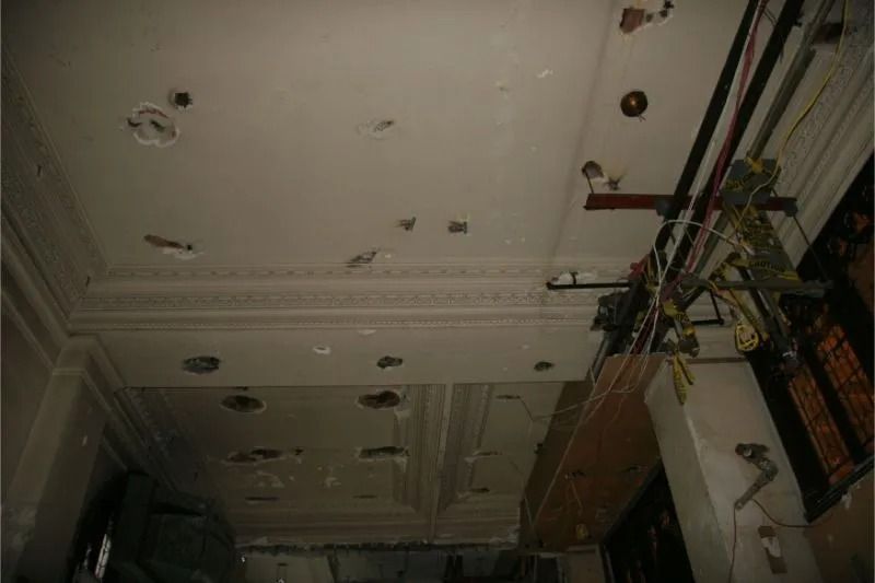 Damaged ceiling with multiple holes and exposed wiring in a dim interior room