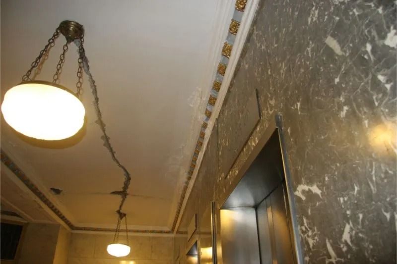 Dim hallway with hanging ceiling lights and a marble-patterned wall beside an elevator.