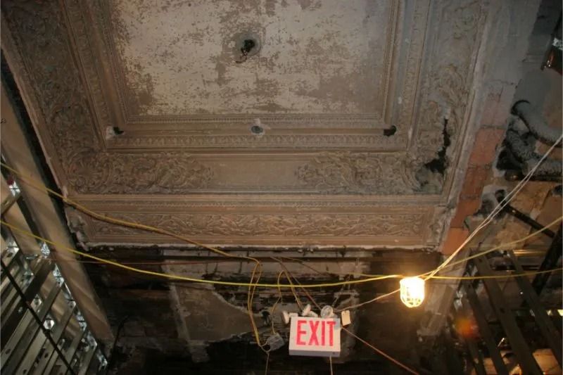 Damaged ornate ceiling with exposed wires and hanging light above an EXIT sign