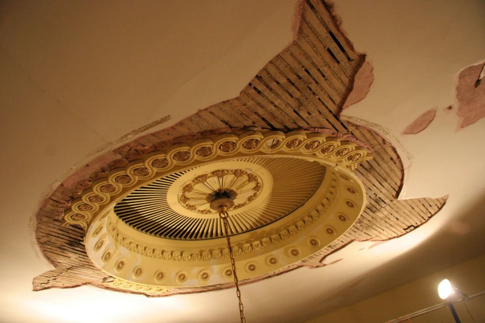 Ornate circular ceiling medallion with gold and beige decorative patterns and exposed plaster around it