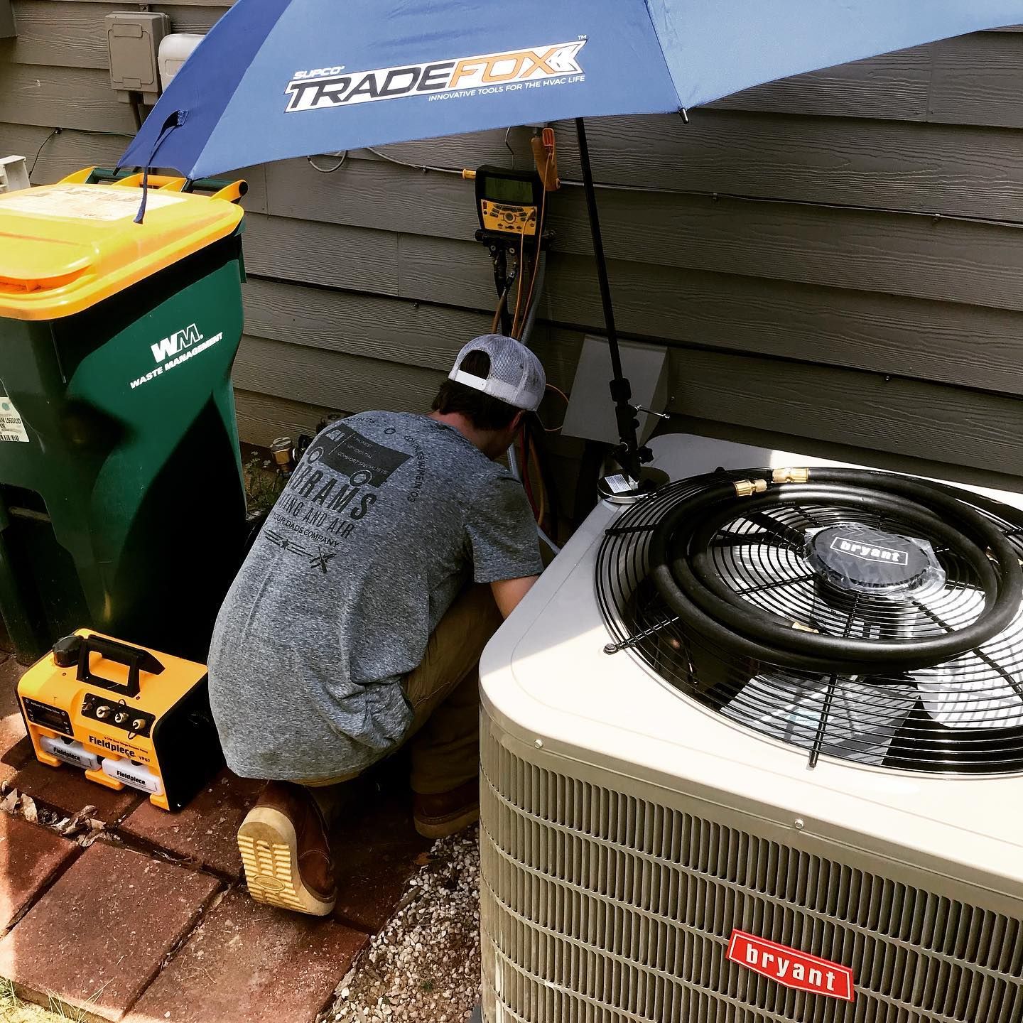 A man is working on an air conditioner under an umbrella.