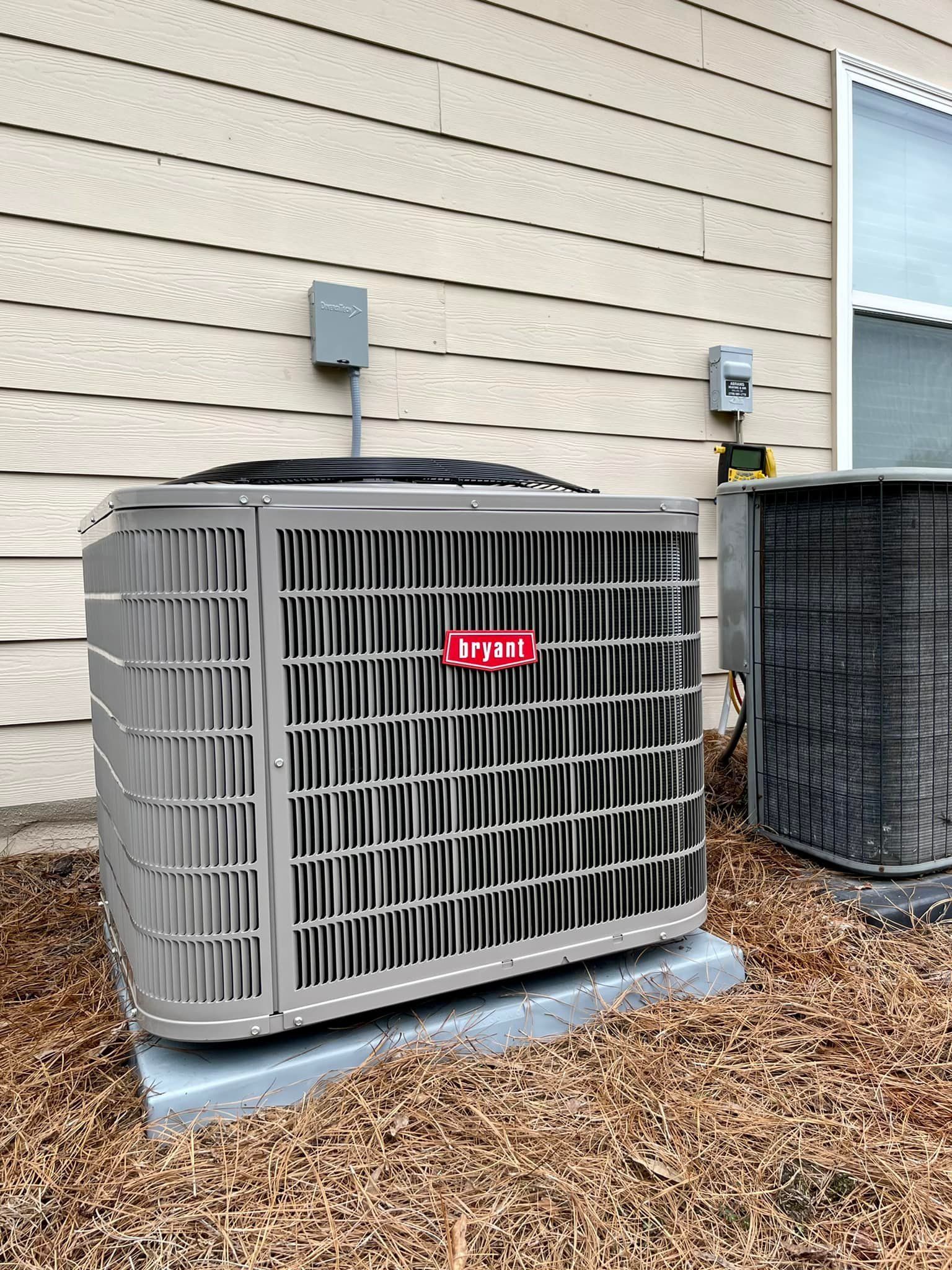 A large air conditioner is sitting outside of a house next to a window.