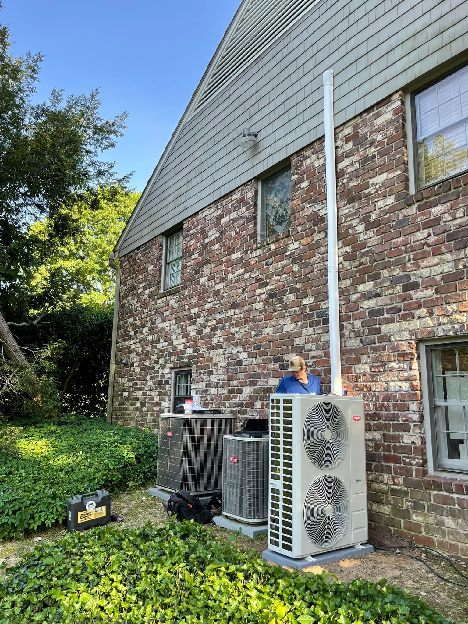 A man is working on an air conditioner on the side of a brick building.